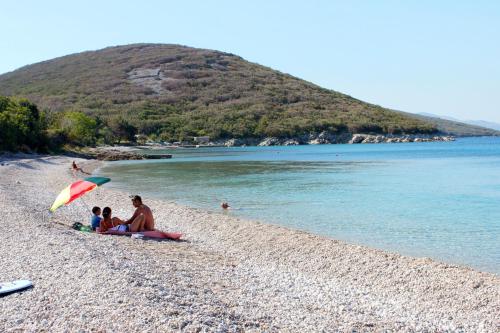 a group of people sitting on a beach with an umbrella at Apartments by the sea Cove Merascica, Cres - 8071 in Štivan