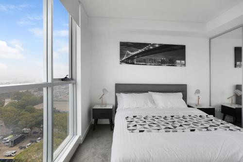 a white bedroom with a bed and large windows at KULA Sydney Airport in Sydney