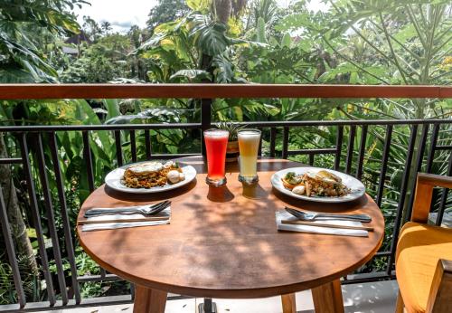 Una mesa con dos platos de comida y bebidas en un balcón. en Gunung Merta Bungalows, en Ubud