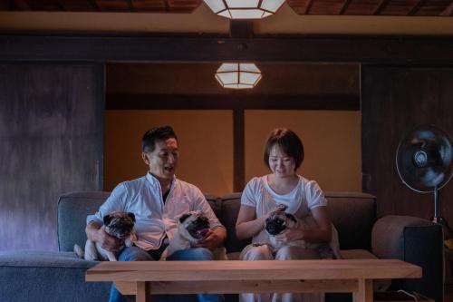 a man and a woman sitting on a couch with two dogs at Kominkayado LOOF Sannoie in Koike
