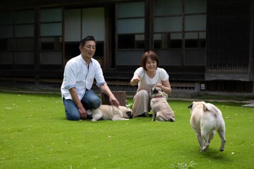 a man and a woman sitting on the grass with two dogs at Kominkayado LOOF Sannoie in Koike