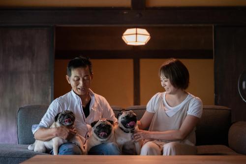 a man and a woman sitting on a couch with four puppies at Kominkayado LOOF Sannoie in Koike