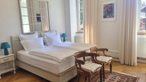 a bedroom with a bed with two chairs and two windows at Chambres d'Hôtes du Marché aux Grains in Bouxwiller