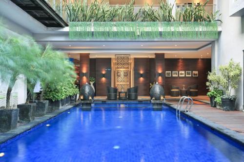 a large swimming pool in a hotel with plants at Ohana Hotel Kuta in Kuta