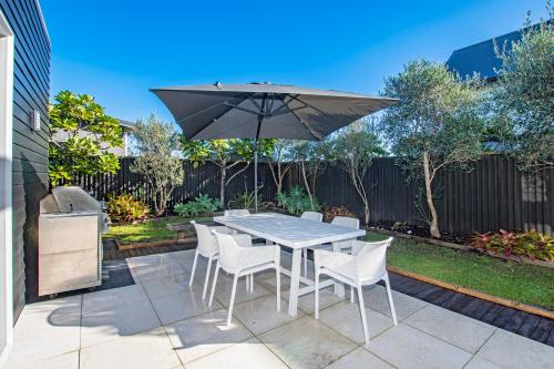 a table and chairs with an umbrella on a patio at Beachy on Bream - Ruakākā Holiday Home in Ruakaka