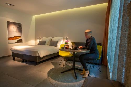 a woman sitting at a table with a laptop in a hotel room at Marcel de Gand Business & Travel in Ghent