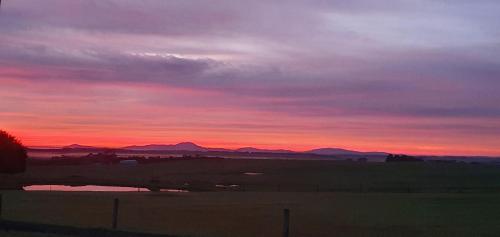 a sunset over a field with mountains in the background at Buln Buln Cabins in Yanakie