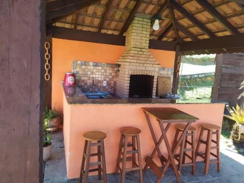 a outdoor kitchen with stools and a counter with a fireplace at Recanto Cravo e Canela in Itatiaia