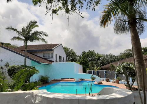 a swimming pool in front of a house with palm trees at Umuzi Guest House in Richards Bay