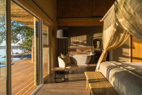 a bedroom with a bed and a balcony with a tub at Victoria Falls River Lodge in Victoria Falls