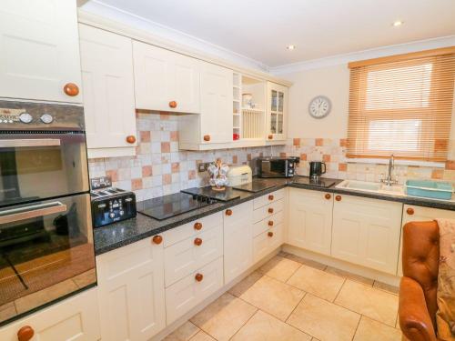 a kitchen with white cabinets and black counter tops at Morannedd in Llanfairpwllgwyngyll
