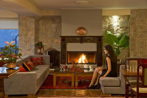 a woman sitting in a living room with a fireplace at Ellinon Thea Arachova in Arachova