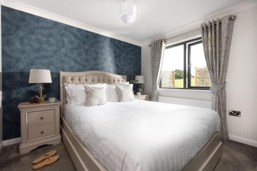 a bedroom with a white bed with a blue accent wall at Blossom Lodge, 1 Roadford Lake Lodges in Lifton