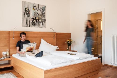 Ein Mann, der auf einem Bett sitzt und eine Zeitschrift liest. in der Unterkunft Hotel Vötterl in Grossgmain