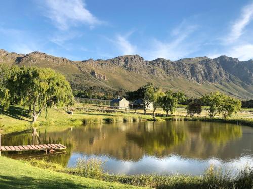 a lake with a house and mountains in the background at Jardin de la Ferme in Franschhoek