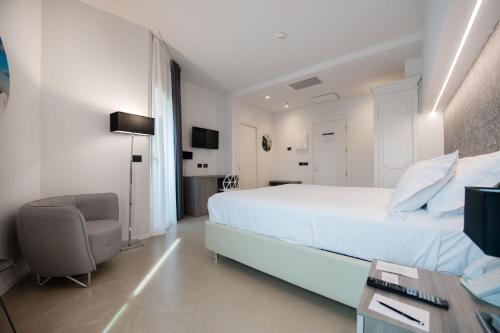 a white bedroom with a bed and a chair at Grand Hotel Faraglioni in Acitrezza