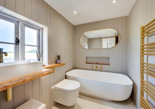 Fairstead في Spexhall: حمام مع حوض استحمام أبيض كبير ومرآة