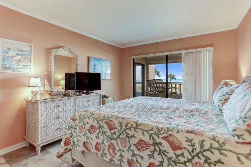 a bedroom with a bed and a television and a balcony at Stay Better Vacations Amelia Island-Oceanfront Surf & Racquet C109 in Fernandina Beach