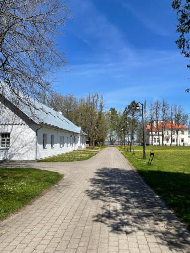 a dirt road leading to a white building and grass at A. Smetonos Dvaro Smetonienės svetainė in Lėnas