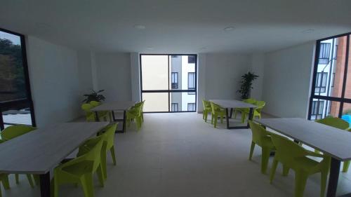 a room with tables and green chairs and windows at Club residencial santafe in Cartago