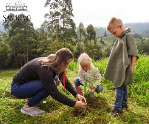a woman and two children planting a plant in a field at Hotel Rural SAN REMO in Santa Rosa de Cabal