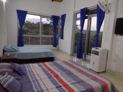 1 Schlafzimmer mit 2 Betten und einem Fenster mit blauen Vorhängen in der Unterkunft FINCA LA AMISTAD in Anapoima