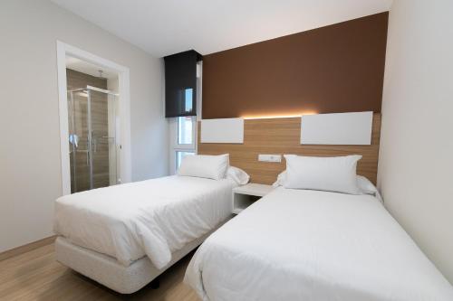 2 Betten in einem Hotelzimmer mit weißer Bettwäsche in der Unterkunft Palacios 30, Playa Nanín in Sanxenxo
