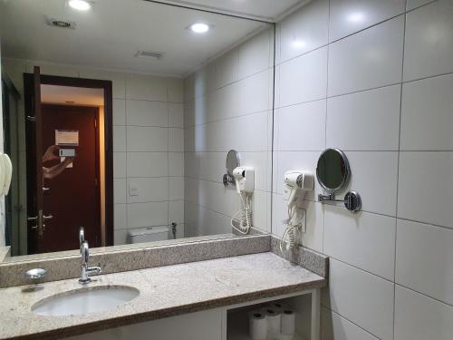 a bathroom with a sink and a mirror with a person taking a picture at Flat Beach Class Internacional in Recife