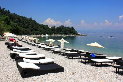 a row of lounge chairs and umbrellas on a beach at Rooms by the sea Medveja, Opatija - 7775 in Lovran
