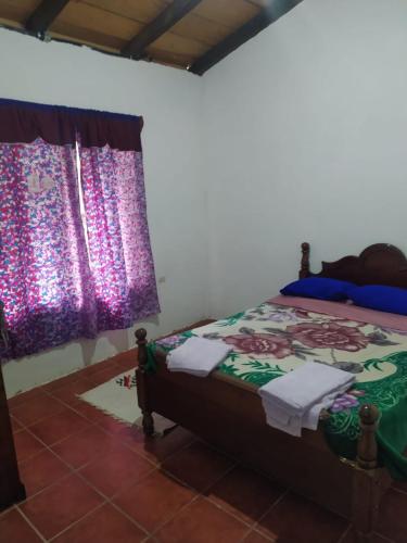 a bedroom with a bed and a window with purple curtains at Hostal El Calvario del Bosque, Aldea Las Cruces, Cobán 