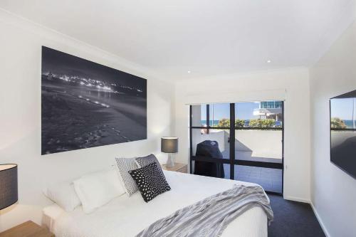 a white bedroom with a bed and a large window at Beachfront 2 in Mollymook