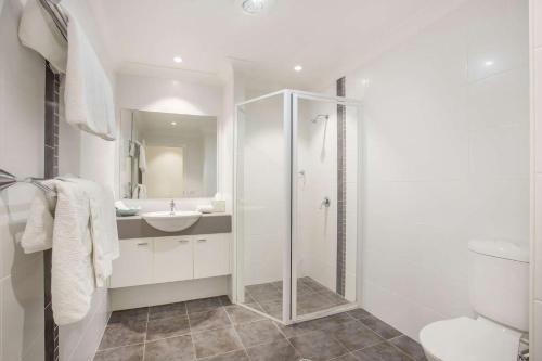 a white bathroom with a shower and a sink at Beachfront 2 in Mollymook