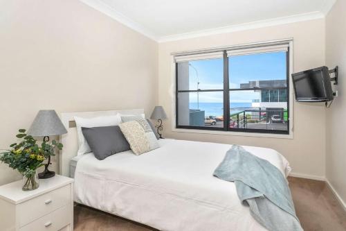 a bedroom with a white bed and a window at Beachfront Five in Mollymook