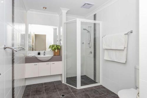a white bathroom with a shower and a sink at Beachfront Five in Mollymook