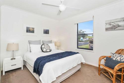a white bedroom with a bed and a window at Beachfront Six in Mollymook