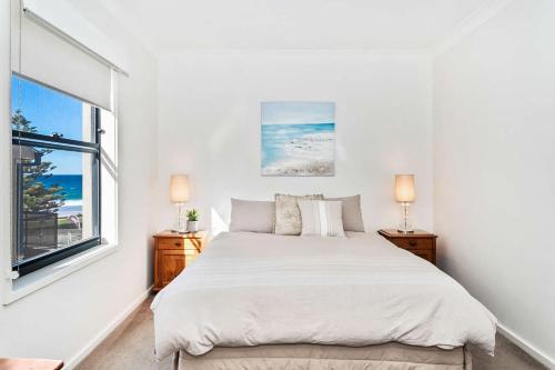 ein weißes Schlafzimmer mit einem Bett und einem Fenster in der Unterkunft Beachfront Four in Mollymook