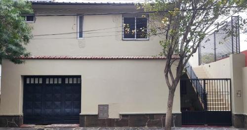 una casa blanca con una puerta negra y un árbol en Alquiler Céntrico Catamarca en San Fernando del Valle de Catamarca