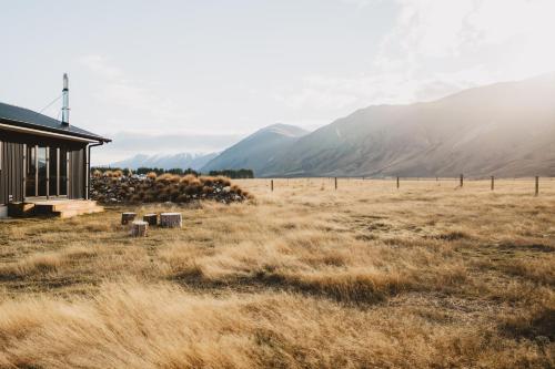 a house in a field with mountains in the background at Peak View Cabin - Ben Ohau - Stylish Seclusion in Twizel