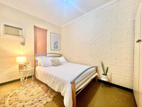 um quarto com uma cama e uma parede de tijolos brancos em Neat 2 bedroom apartment, with free parking em South Hedland
