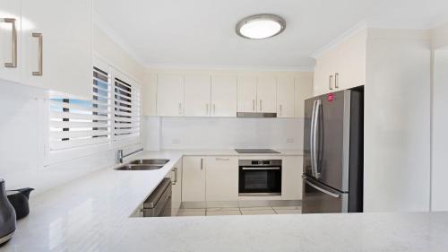 a kitchen with white cabinets and a stainless steel refrigerator at Surfspray 4 Pebbly Beach in Forster