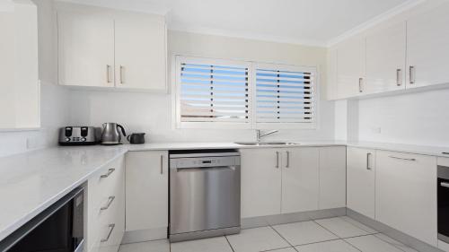 a white kitchen with white cabinets and a window at Surfspray 4 Pebbly Beach in Forster
