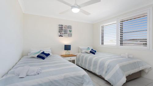 two beds in a white room with a window at Surfspray 4 Pebbly Beach in Forster