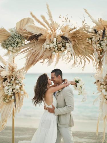 a bride and groom kissing under a floral arch on the beach at Patina Maldives, Fari Islands in North Male Atoll