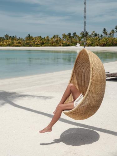a woman sitting in a swing on a beach at Patina Maldives, Fari Islands in North Male Atoll