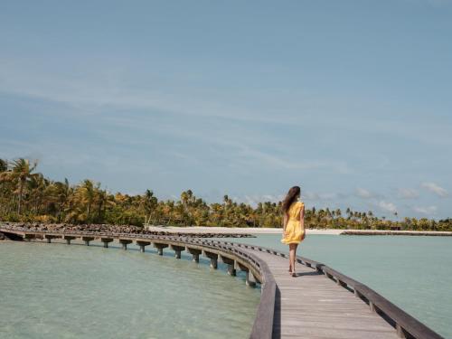 a woman walking on a wooden bridge over the water at Patina Maldives, Fari Islands in North Male Atoll