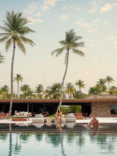 two people sitting in a swimming pool with palm trees at Patina Maldives, Fari Islands in North Male Atoll