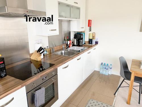 cocina con armarios blancos, fregadero y mesa en Travaal.©om - 2 Bed Serviced Apartment Farnborough, en Farnborough