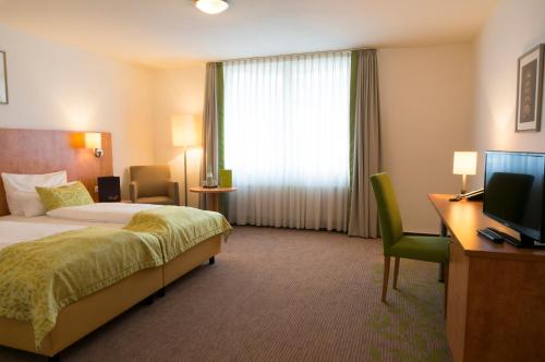 Habitación de hotel con cama, escritorio y TV. en Hotel Mingarden en Düsseldorf