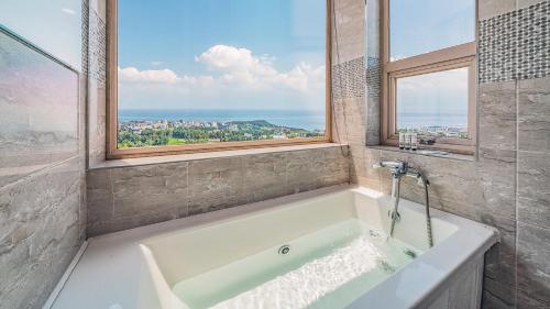 baño con bañera blanca y ventana en J View Hotel, en Seogwipo