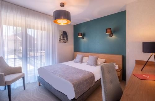 a bedroom with a bed and a chair and a window at The Originals City, Hôtel Les Thermes de l'Avenue, Dax in Dax